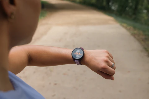 Biegaczka stojąca na polnej ścieżce i patrząca na dane na swoim zegarku Garmin Forerunner 165 na lewym nadgarstku.